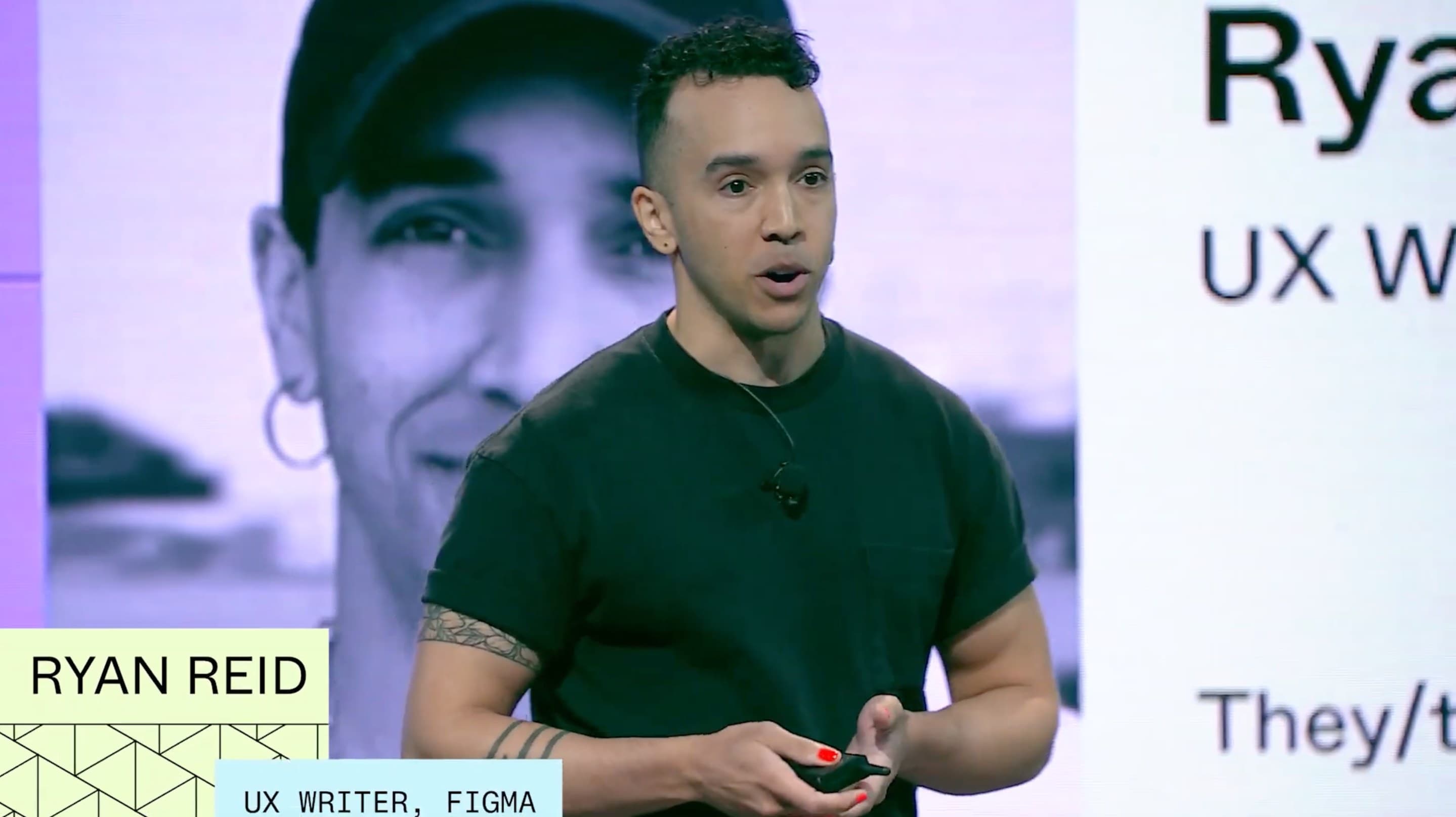 Ry presenting in a black tee, in front of a slide carrying their own portrait beside “Ryan Reid — UX Writer, Figma, they/them”, with the same name and title repeated in lower-third captions